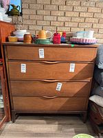 Front view of walnut tallboy dresser with four drawers and integrated curved pulls; various dishes on top.