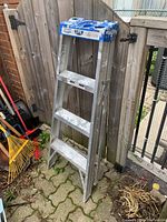 Full view of the Lite aluminum 4-step ladder leaning against a wooden fence showing the ladder's height and condition.