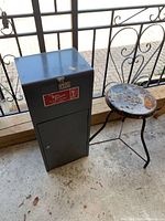 Front view of metal storage cabinet and rusted metal stool on concrete floor.