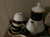 Coffee pot and stacked matching cups and saucers in Noritake Valhalla B pattern, showing black band and gold trim