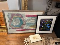 Photo showing all three framed artworks: a larger geometric abstract painting, a colorful painting with bold shapes, and a small framed etching on the floor.
