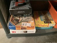 Image showing six puzzle boxes stacked on a shelf, with one Balderdash game box on top, puzzles include 1000 and 2000 piece versions and various images including Windsor Castle panorama.