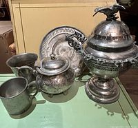 Full view of all serving ware items including the lidded serving bowl with hummingbird, teapot, cups, and plate on green tabletop.