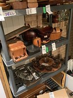 Photo showing gray plastic shelving unit with four shelves containing various wooden decorative bowls, trays, glass items (not included in lot). Shelving unit stands against brick wall.