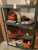 Photo showing grey plastic four-tier shelving unit with various household items stored on shelves, some shelves visibly bent and worn.