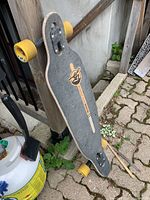 Full longboard skateboard showing top grip tape, truck and yellow wheels resting on ground.
