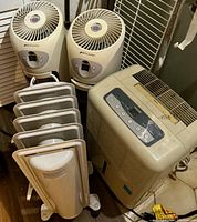 Lot showing 2 Bionaire humidifiers, Honeywell oil-filled radiator space heater, and Forest Air dehumidifier. Items are grouped on a floor with visible wear and dust, needing cleaning.