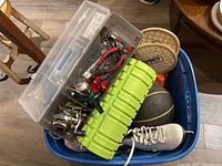 All items packed in blue plastic storage bin showing skates, foam roller, Wilson basketball, racquetball rackets, fishing tackle box, and water bottle.