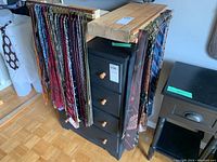 Photo of men's neckties hanging on a metal rack attached to a black chest of drawers, showing various colors and patterns