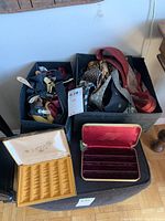Boxes containing assorted ties and suspenders along with two open jewelry boxes on a black stand