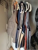 View of vests hanging in a row on white hangers, showcasing different colors and fabric textures including tweed, velvet, and striped cotton.