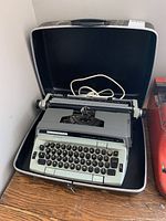 Vintage Eaton Viking Cartridge-Automatic 12 electric typewriter housed inside a hard black travel case with the lid open showing the machine and the unplugged white power cord.