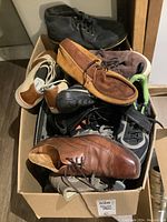 Box filled with assorted men's vintage shoes including dress shoes, sneakers, moccasins, suede boots and running shoes.