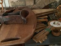 Wooden kitchenware items including a large curved cutting board with handle cutouts, a dark wood bowl, a wooden rack with grooves, and a circular wooden wall plaque with a rooster tile inset.