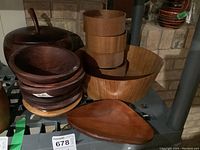 Wide view of the assortment showing large teak salad bowl, stacked medium teak serving bowls, dark wood apple-shaped bowl, and lidded wooden bowl.
