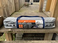 Photo of the tent packed in a gray carrying bag with blue handles and black and orange label stating brand and tent details