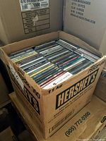Box filled with multiple rows of CDs, showing spines and cases packed closely in a Hershey's branded cardboard box.