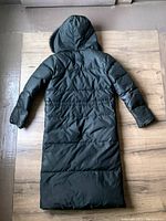 Full view of the coat laid flat showing the back with hood up on wooden floor