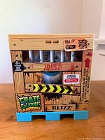 Photo of Crate Creatures Surprise toy crate box designed with wood panel print, caution labels, and visible monster eyes and fur behind bars, blue pallet base