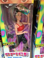 Front view of Mel B Barbie doll in original sealed box with visible accessories inside.