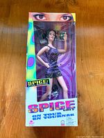 Photo of boxed Spice Girls Barbie doll dressed in purple sequined dress, holding a microphone prop with box showing colorful psychedelic design and Barbie logo.