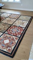 Photo showing close-up of rug corner with floral and geometric patterns in various colors on wooden floor.