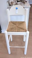 Full view of the white painted wooden bar stool with woven wicker seat, showing front and seat details.