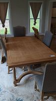 Wood dining room table set up with chairs, rectangular shape, paneled top, wooden carved legs and cross supports visible