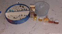 Photo showing blue jewelry box with various earrings inside, small bottles of perfume and a glass bowl with cat-shaped lid nearby.