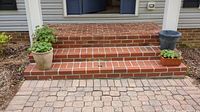 Front view of two planters on brick steps: large dark round planter and rectangular terracotta planter with green plant.