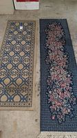 Photo showing two runner rugs side by side on the floor. Left rug is beige with blue geometric pattern, right rug is dark blue with floral design.