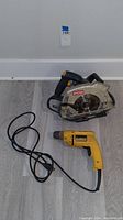 Full view of Ryobi circular saw and DeWalt electric drill on floor with lot tag