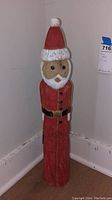 Full view of wooden Santa statue standing on floor next to wall, showing full length and overall condition.
