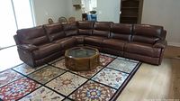 Full view of the brown faux leather sectional couch arranged in an L shape with a glass-top wooden coffee table in front.