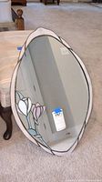 Front angle view of the oval mirror showing the stained glass floral design and reflective surface.