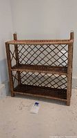 Full front view of the wicker wall shelf placed against a wall showing three shelves and lattice pattern.