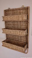 Wicker wall shelf showing the three woven wicker baskets and backboard from a side angle.