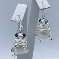 Front angled view of frog earrings showing the pearl bodies and black spinel eyes with silver hooks