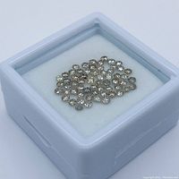 White plastic jeweler’s box containing multiple small brown diamonds on a white pad