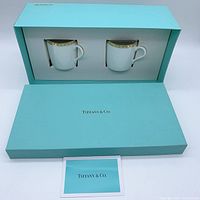 Two Tiffany & Co. cups and saucers in original light blue Tiffany box alongside paperwork.