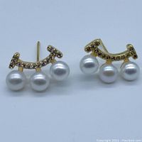 Front view of both earrings laid flat showing gold plated arches with clear stones and three white pearls each