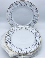 Two Tiffany & Co. Dancing 'T' plates standing and lying flat showing overall design and rim detail with blue logos and gold trim.