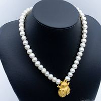 Frontal view on black bust showing pearl strand and beetle pendant