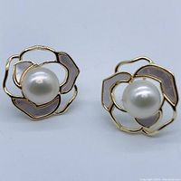 Front view of a pair of floral design stud earrings with a central natural pearl and shell inlays on petals, set in 18K yellow gold plated metal.