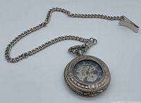 Oblique view of watch face and attached curb chain with clip on white background