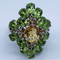 Front view of ring showing oval citrine center stone surrounded by green peridot stones and small blue sapphire accents set in 925 sterling silver with white gold plating.
