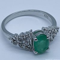 Front angle view showing oval emerald center and white topaz clusters