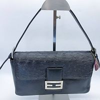 Front angle of black genuine ostrich leather bucket shoulder bag showing textured ostrich leather flap and silver hardware buckle front clasp with one shoulder strap.