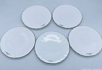 Top view of five white scalloped edge plates with gold trim and Givenchy Paris logos on front