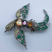 Top view showing oval citrine on the body, pinkish rhodolite garnet and orange garnet, green emerald stones on wings and tail, and smaller yellow accent stones on wings.